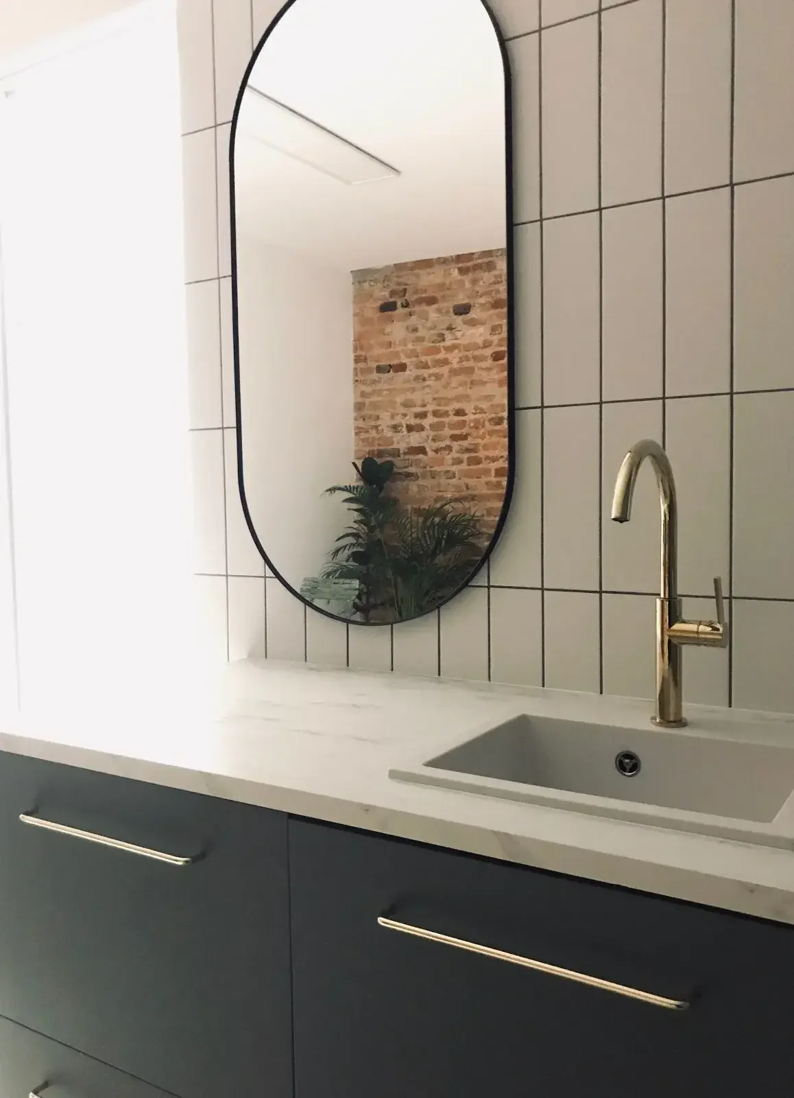 Lavabo con grifo dorado y espejo ovalado sobre azulejos blancos