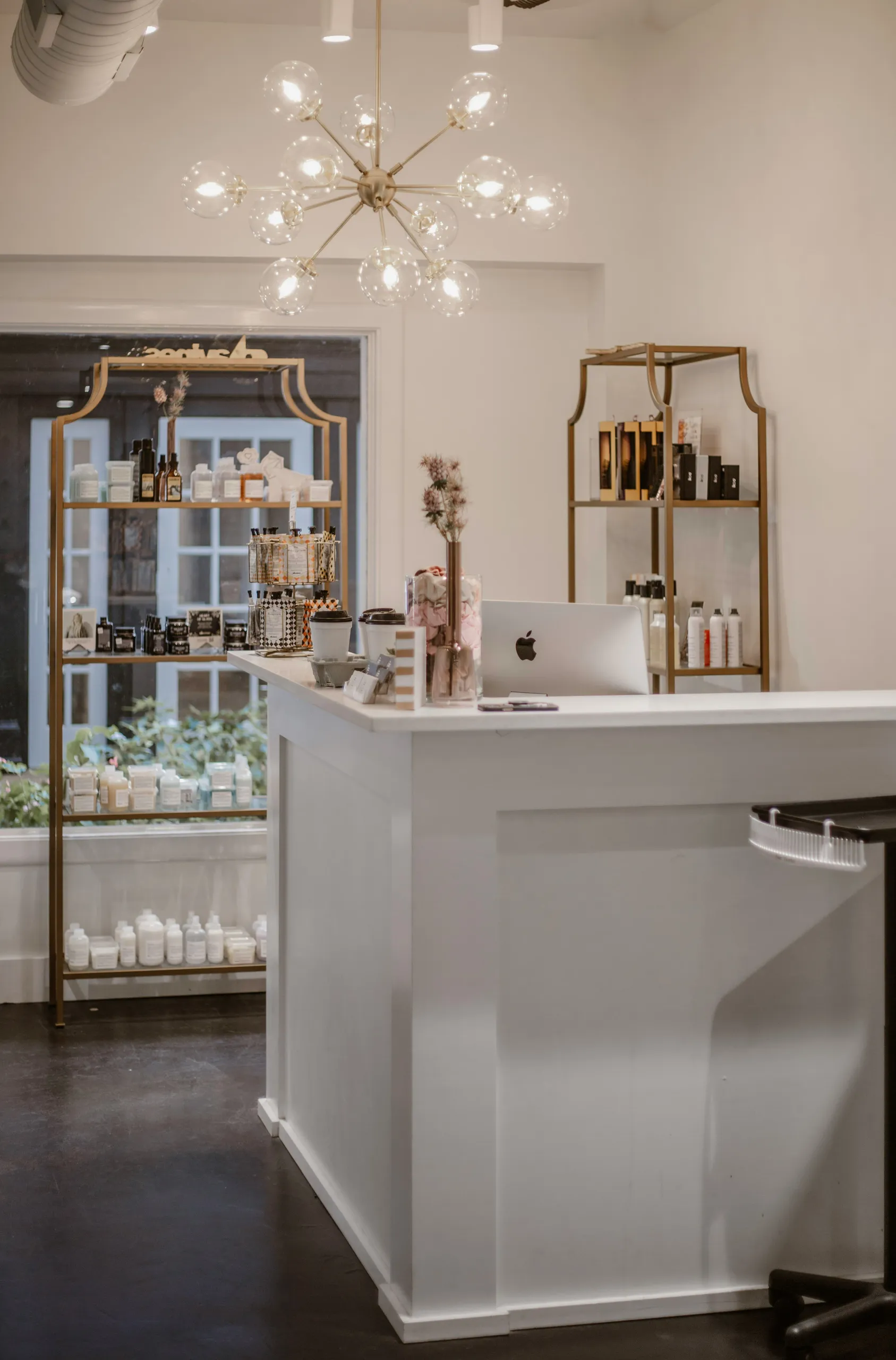 Recepción del salón con mostrador claro, estanterías doradas y cosméticos